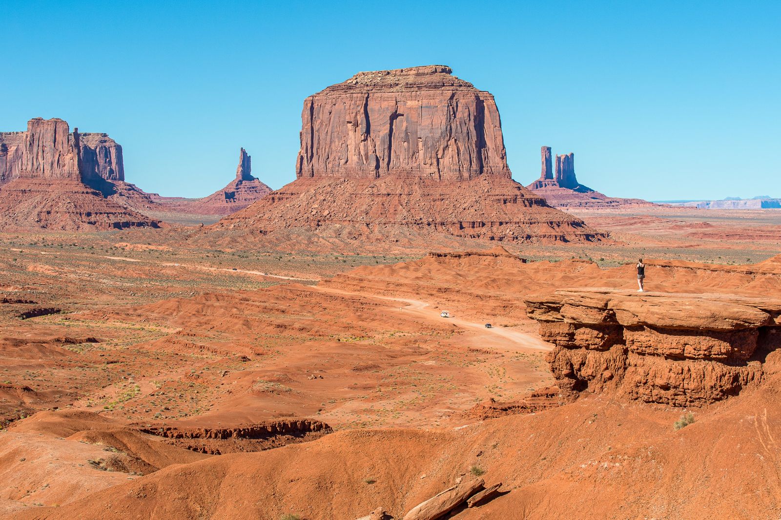 Red buttes and mesas across the valley floor from a rock ledge