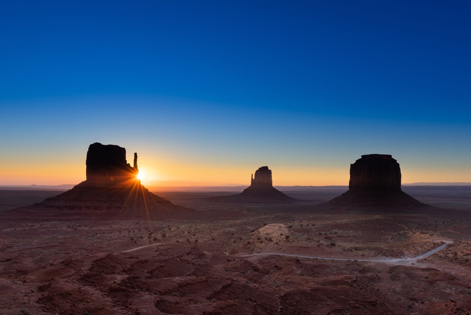 The sun rising behind the silhouetted Mitten buttes